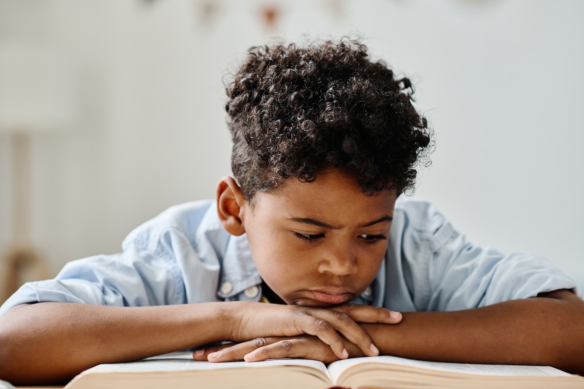 Serious African boy concentrating on reading a book at table at home